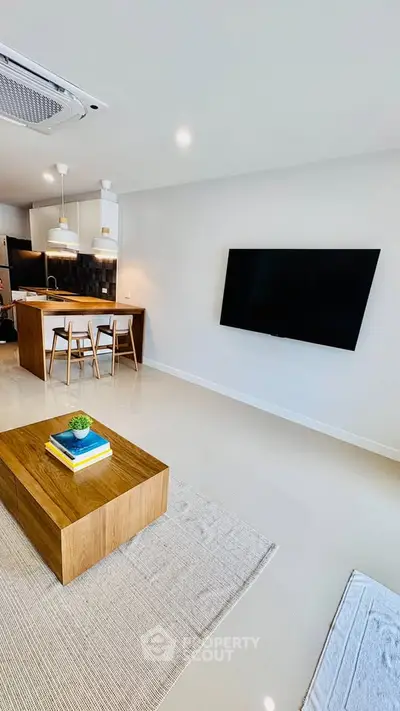 Modern living room with open kitchen, sleek TV setup, and stylish wooden furniture.