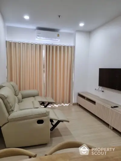 Spacious and well-lit living room with comfortable recliner sofa, modern entertainment unit, and elegant beige curtains complementing the neutral color palette.