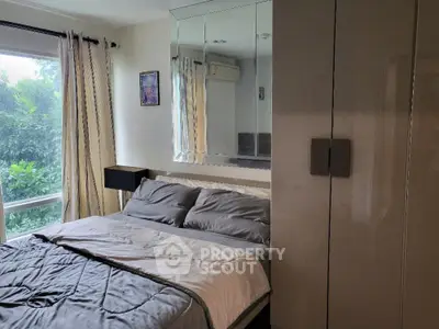 Cozy bedroom with large window and modern decor, offering a serene view of lush greenery.
