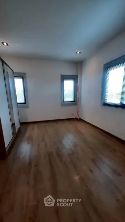 Spacious empty bedroom with wooden flooring and large windows for natural light.