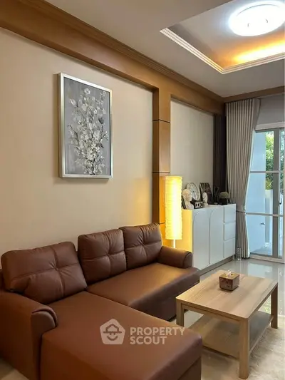 Elegant living room with brown leather sofa, modern decor, and natural light from large window.