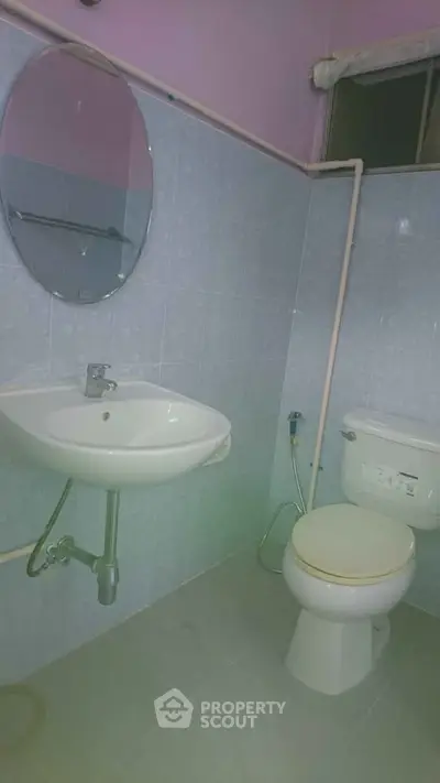 Compact bathroom with sink, toilet, and round mirror in a tiled setting.