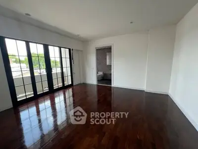 Spacious empty room with polished wooden floors and large windows opening to a balcony.
