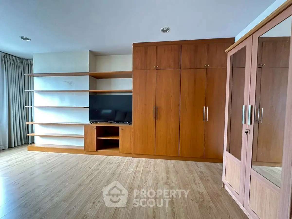 Spacious bedroom with built-in wooden wardrobe and modern shelving unit.