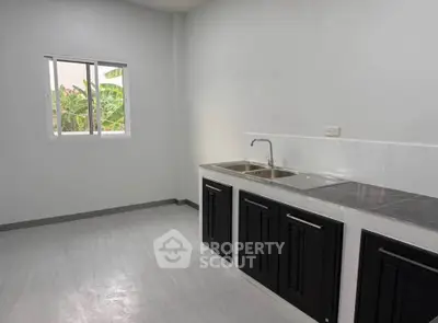 Modern kitchen with sleek black cabinets and dual sink, featuring a bright window view.