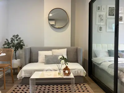 Modern living room with stylish decor and cozy ambiance, featuring a sofa and glass partition leading to a bedroom.