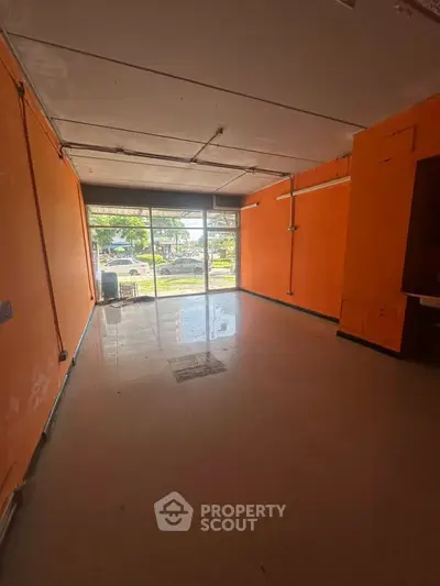 Spacious commercial space with large front windows and vibrant orange walls.