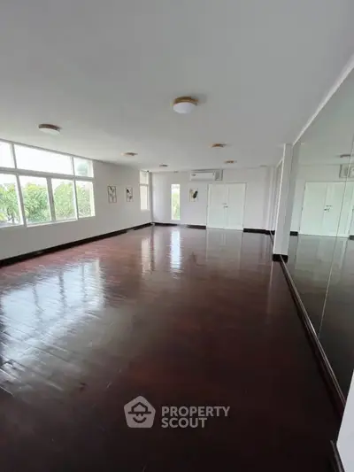 Spacious empty room with large windows and polished wooden floors, ideal for customization.