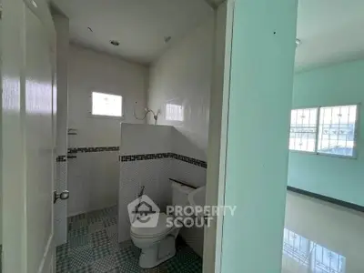 Compact bathroom with tiled walls and window, adjacent to a bright room with large windows.