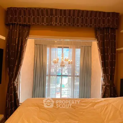 Luxurious bedroom with elegant drapes and chandelier overlooking a stunning city view.