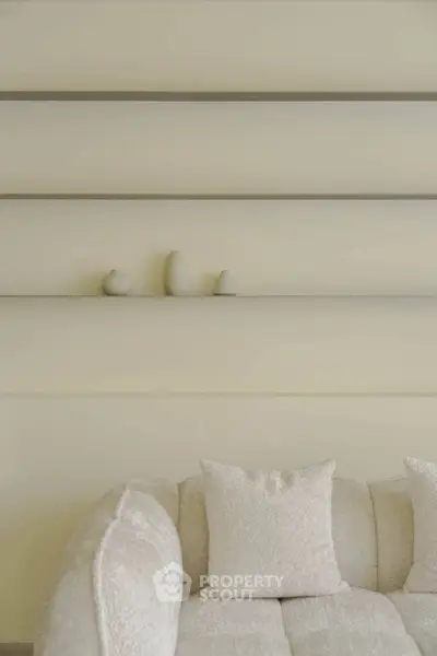 Elegant modern living room with plush white sofa and minimalist decor on sleek wall shelves.