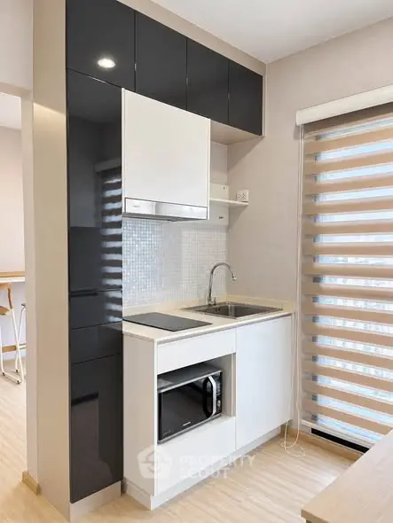 Modern compact kitchen with sleek black and white cabinetry, featuring a built-in microwave and stylish blinds.