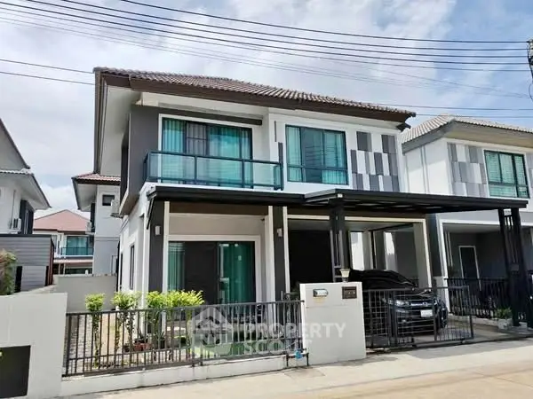 Modern two-story house with balcony and carport in suburban neighborhood.