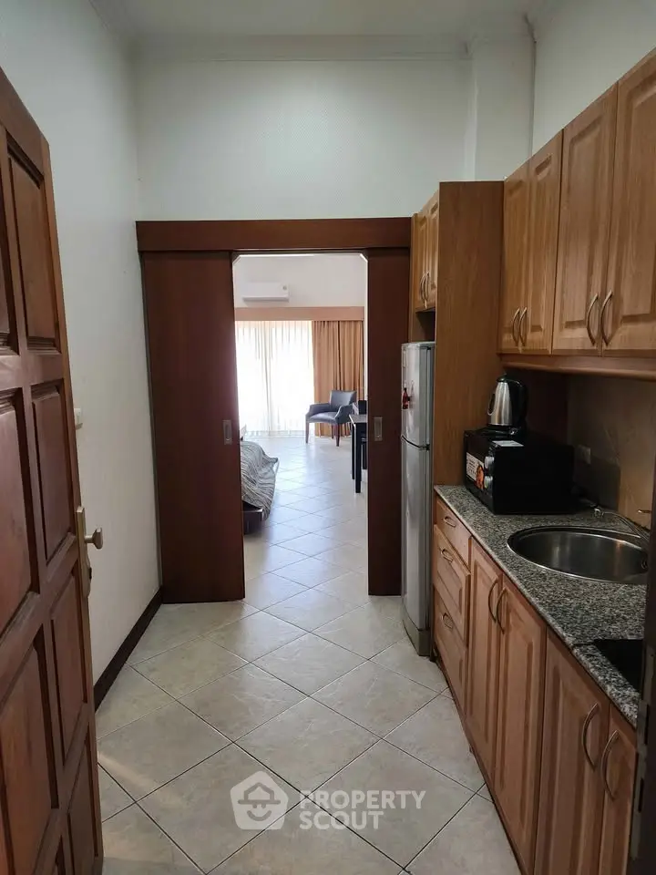 Spacious kitchen with wooden cabinets leading to a bright living area