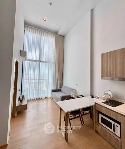 Modern high-ceiling living room with kitchenette and large windows offering city views.