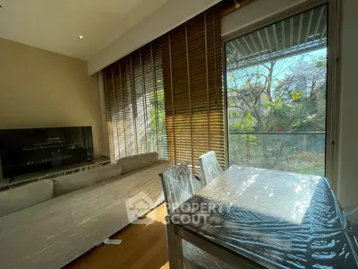 Modern living room with large windows and garden view, featuring sleek furniture and natural light.