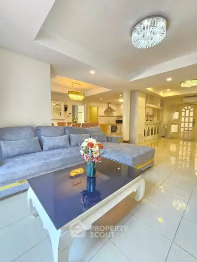 Spacious living room with elegant decor and open kitchen layout, featuring modern lighting and a cozy seating area.