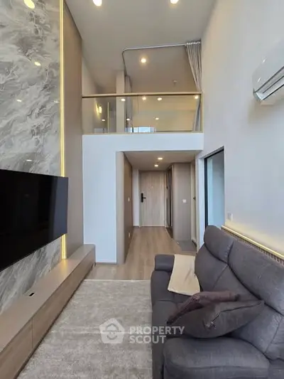 Modern living room with high ceiling and mezzanine, featuring sleek design and cozy seating area.