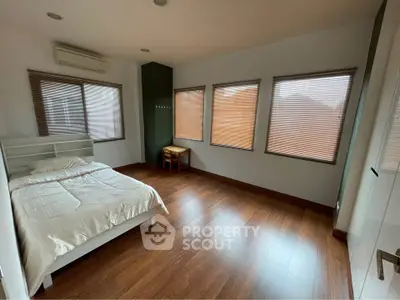 Spacious bedroom with wooden flooring and large windows for natural light.