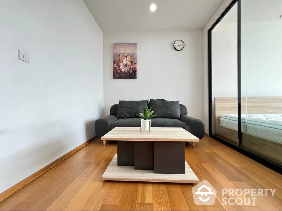 Modern living room with sleek sofa, wooden flooring, and stylish decor adjacent to a cozy bedroom.