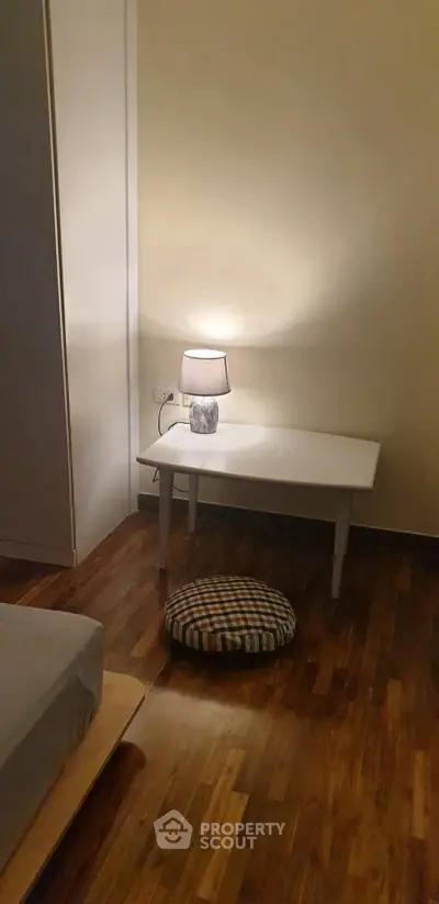 Cozy bedroom corner with wooden flooring and modern lamp on a sleek white table.