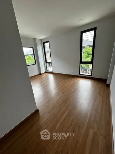 Spacious empty room with wooden flooring and large windows offering natural light and garden views.