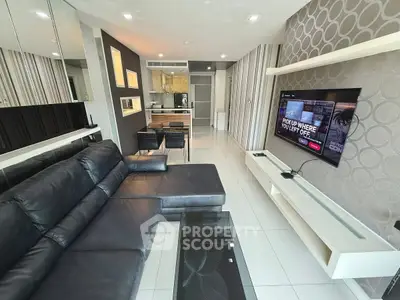 Modern living room with sleek black leather sofa and wall-mounted TV, open kitchen in background.