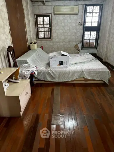 Cozy bedroom with wooden floors and air conditioning, featuring a bed and a bedside table.
