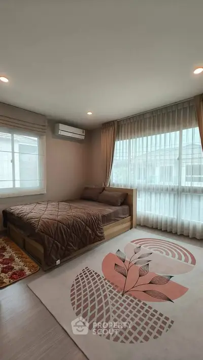 Spacious bedroom with large windows and modern decor, featuring a cozy bed and stylish rug.