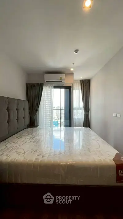 Modern bedroom with large window and city view, featuring a comfortable bed and stylish curtains.