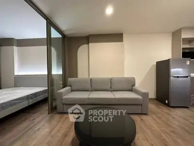 Modern living room with sleek gray sofa and glass coffee table, adjacent to a cozy bedroom.