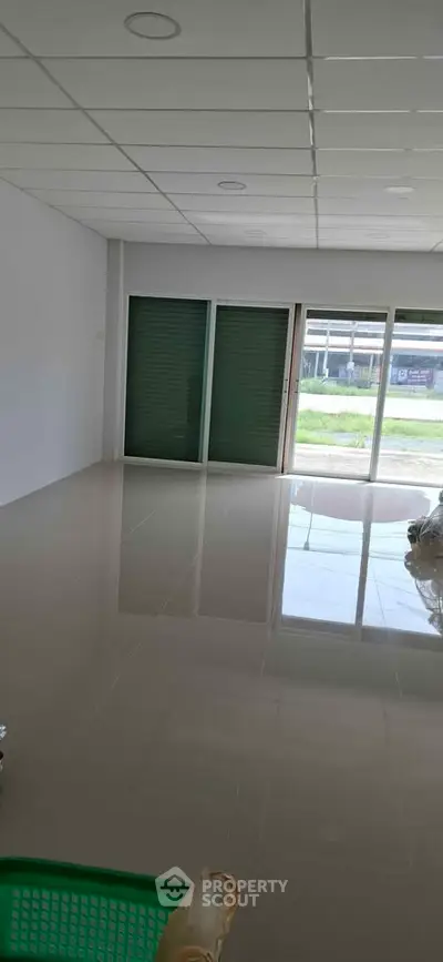 Spacious empty room with glossy tiled floor and large windows offering natural light.