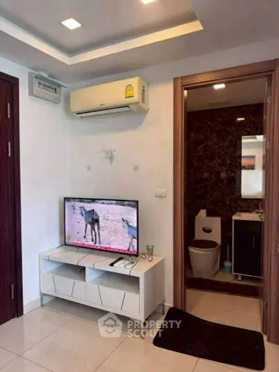 Modern living room with TV and air conditioning, adjacent to a stylish bathroom.