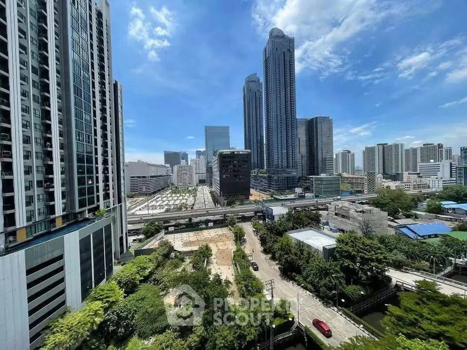 Stunning cityscape view from high-rise building with lush greenery and modern skyscrapers under a clear blue sky.