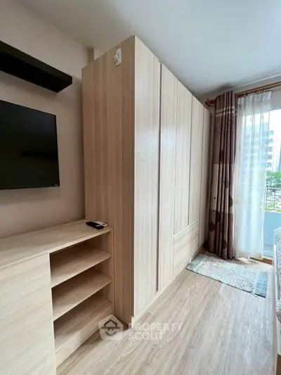 Modern bedroom with built-in wardrobe and TV, featuring a large window with city view.