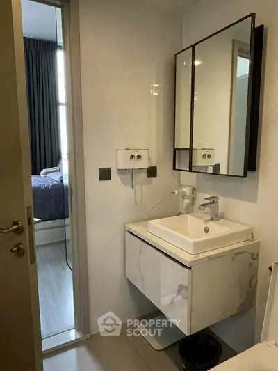Modern bathroom with sleek vanity and mirror, adjacent to a cozy bedroom.