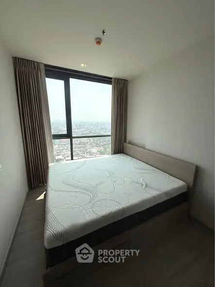 Modern bedroom with large window offering stunning city view, featuring a comfortable bed and elegant curtains.