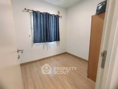 Spacious empty bedroom with wooden flooring and blue curtains, ready for personalization.