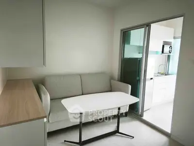 Modern compact living room with sleek sofa and table, adjacent to a bright kitchen area.