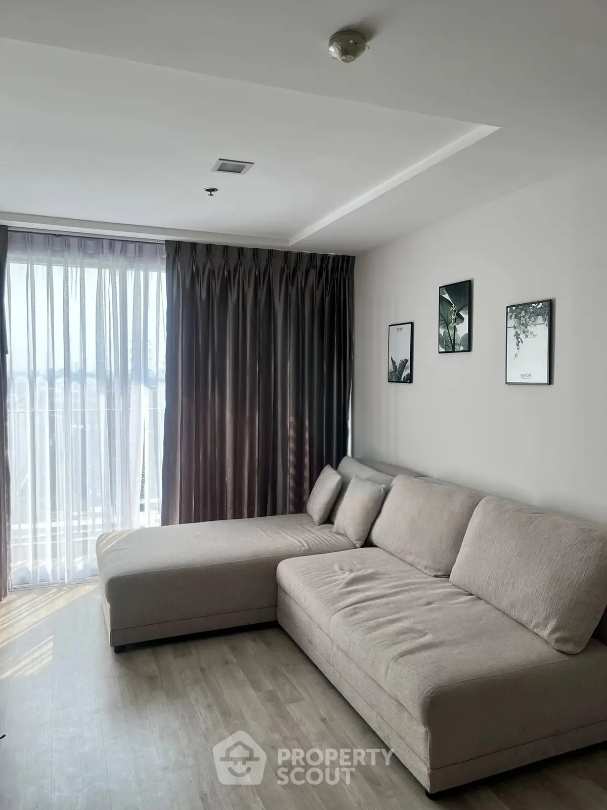 Modern living room with large sofa and floor-to-ceiling windows offering natural light.