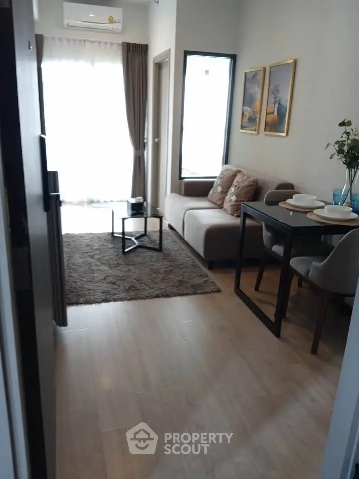 Modern living room with cozy sofa, dining table, and natural light from large window.