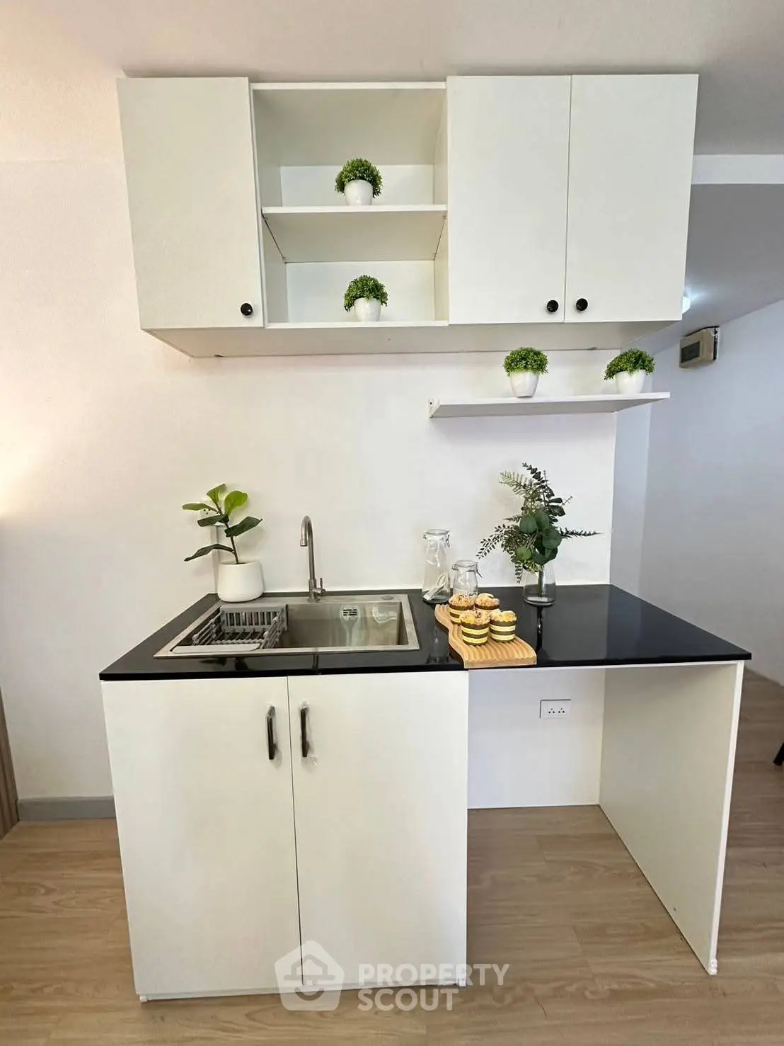 Modern compact kitchen with sleek black countertop and white cabinets, featuring stylish decor and efficient layout.