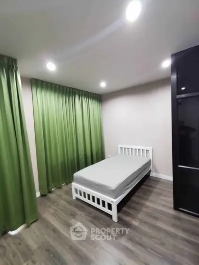 Modern bedroom with green curtains and wooden flooring, featuring a single bed and sleek wardrobe.