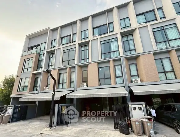 Modern multi-story townhouse with large windows and gated parking area.