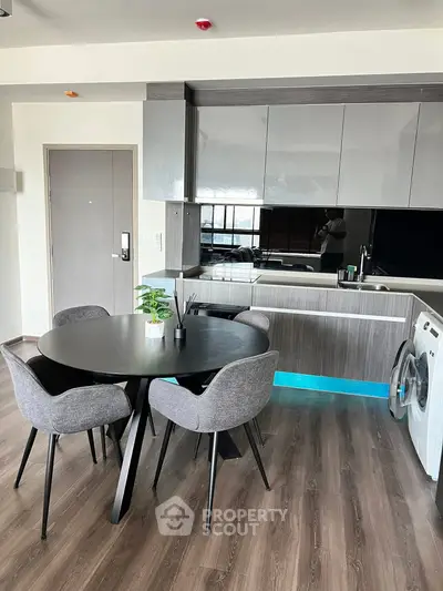 Modern kitchen with sleek cabinetry and dining area, featuring a washing machine and stylish decor.
