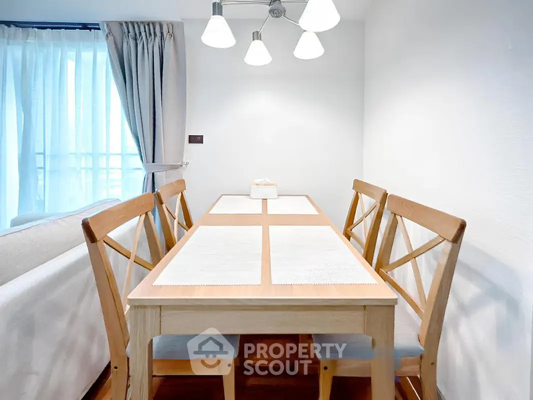 Bright dining area with wooden table and chairs, modern lighting, and natural light from large window.