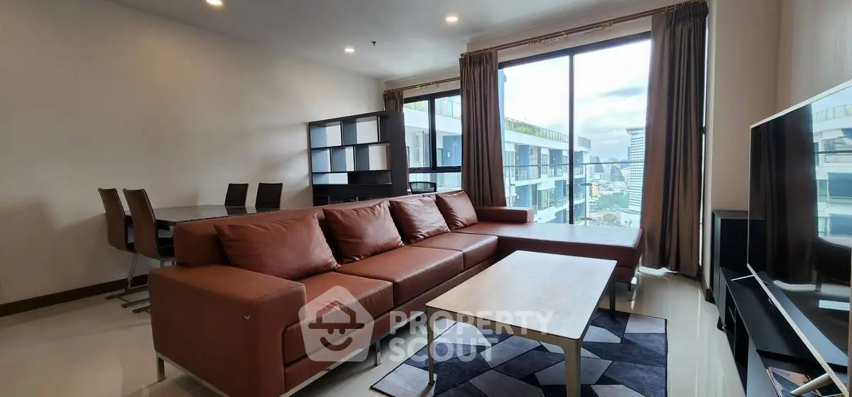 Spacious modern living room with large windows and city view, featuring a stylish brown leather sofa and dining area.