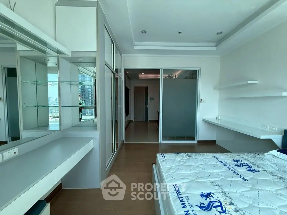 Modern bedroom with sleek design and city view, featuring built-in storage and large windows.