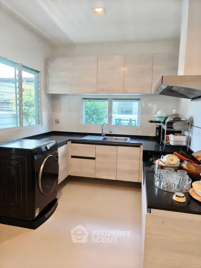Modern kitchen with sleek cabinets, black countertops, and a washing machine, offering a functional and stylish space.