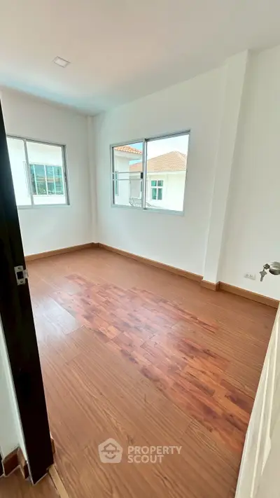 Spacious bedroom with wooden flooring and large windows offering natural light.